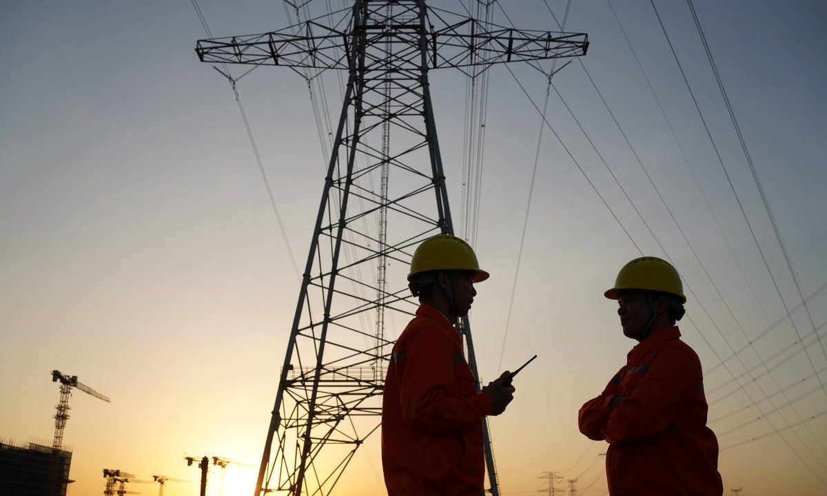 Two workers inspect high-tension power lines.