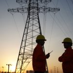 Two workers inspect high-tension power lines.