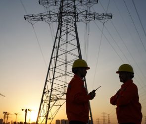 Two workers inspect high-tension power lines.