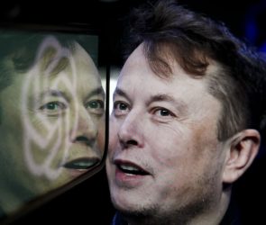In this photo illustration, the logo of 'OpenAI' is displayed on a mobile phone screen in front of a computer screen displaying the photograph of Elon Musk.