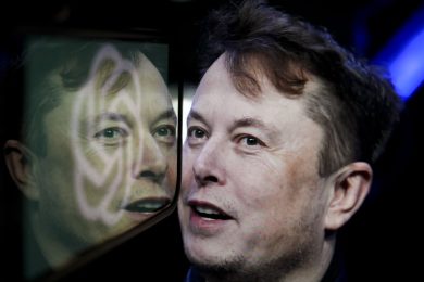 In this photo illustration, the logo of 'OpenAI' is displayed on a mobile phone screen in front of a computer screen displaying the photograph of Elon Musk.