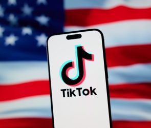 The TikTok app and logo are seen on a mobile device in front of a US flag