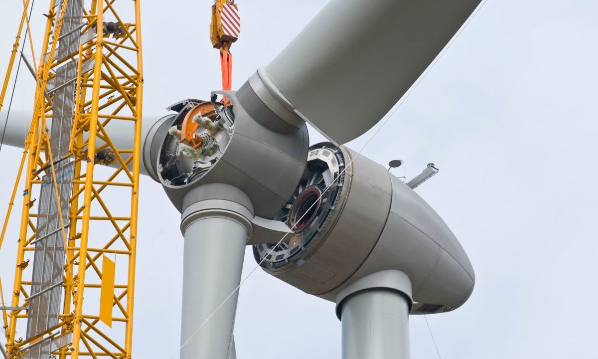 A crane positions the rotor of a wind turbine during construction.