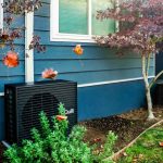 A dark grey heat pump sits outside a blue home.