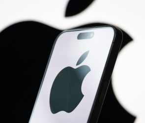 In this photo illustration, the logo of Apple Inc. is displayed on a smartphone screen, with the company's iconic black apple symbol visible in the background.