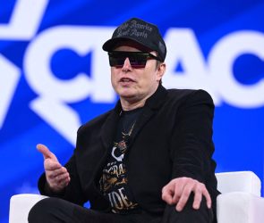 Elon Musk on stage at CPAC in Maryland with sunglasses on and a MAGA hat