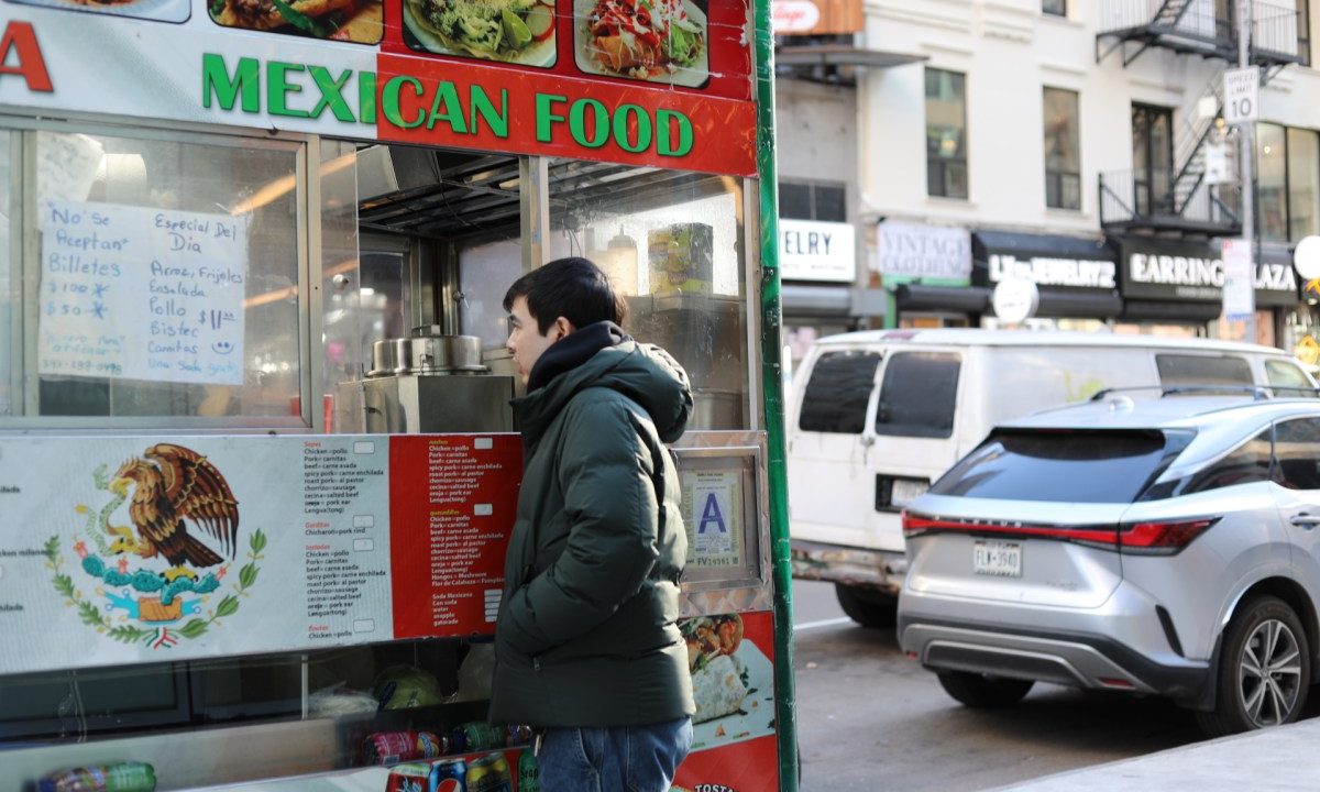A man places an order at a Mexican food cart.