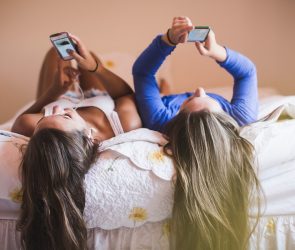 Teenage girls lying on bed looking at smart phones