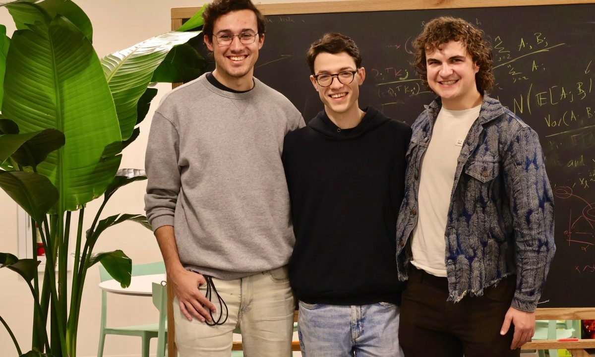 Three smiling men stand in front of a chalkboard