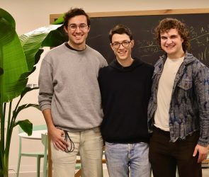 Three smiling men stand in front of a chalkboard