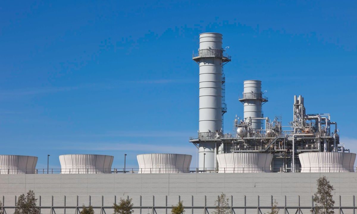 Smoke stacks from a natural gas power plant stand against a blue sky.