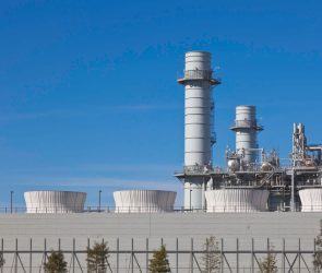 Smoke stacks from a natural gas power plant stand against a blue sky.