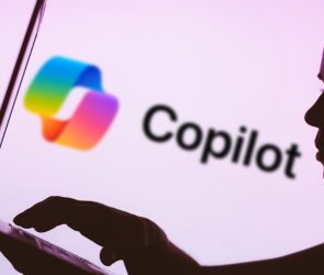 In this photo illustration, the Microsoft Copilot logo is seen in the background next to a silhouette of a person using a notebook.