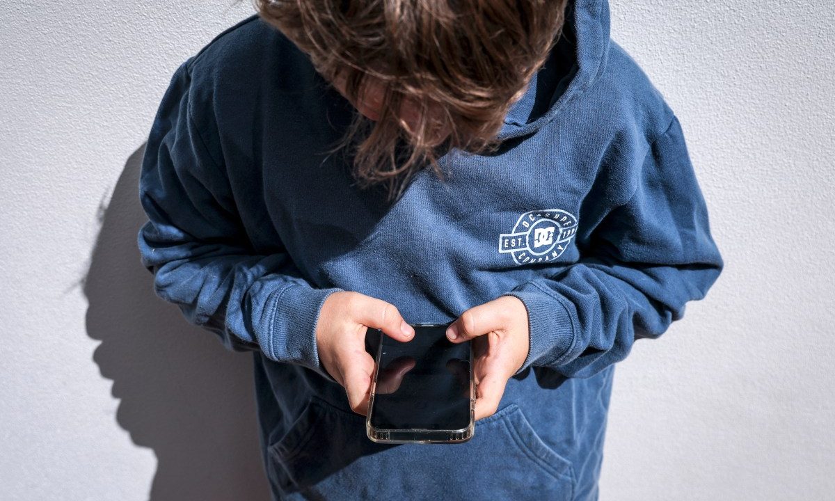Shows a 14-year-old boy as he looks at social media on his mobile phone.