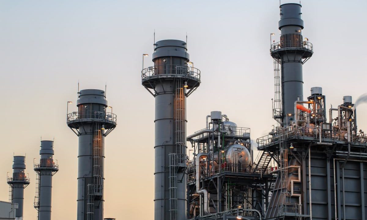 Natural gas power plant smoke stacks stand against a twilight sky.