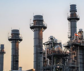 Natural gas power plant smoke stacks stand against a twilight sky.