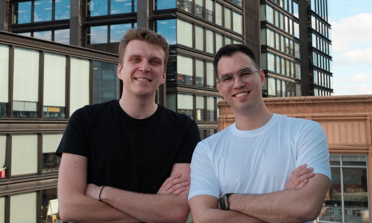 Two men stand on a rooftop, crossing their arms