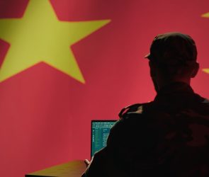 A man sits in front of a computer and the Chinese flag.
