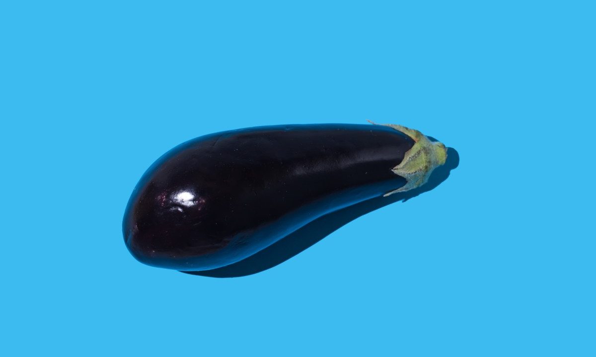 Raw eggplant with hard shadow on blue background.
