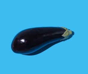 Raw eggplant with hard shadow on blue background.