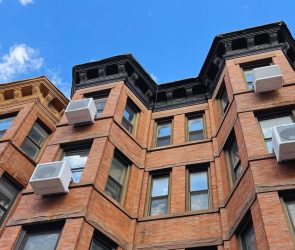 Heat pumps hang on the outside of an apartment building.