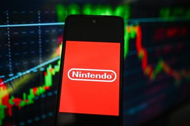Nintendo logo is seen displayed on a smartphone with stock market percentages on the background.
