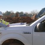 Two workmen look at plans on the hood of a Ford F150
