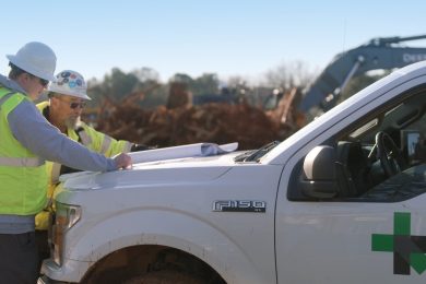 Two workmen look at plans on the hood of a Ford F150