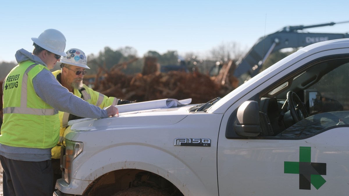Two workmen look at plans on the hood of a Ford F150